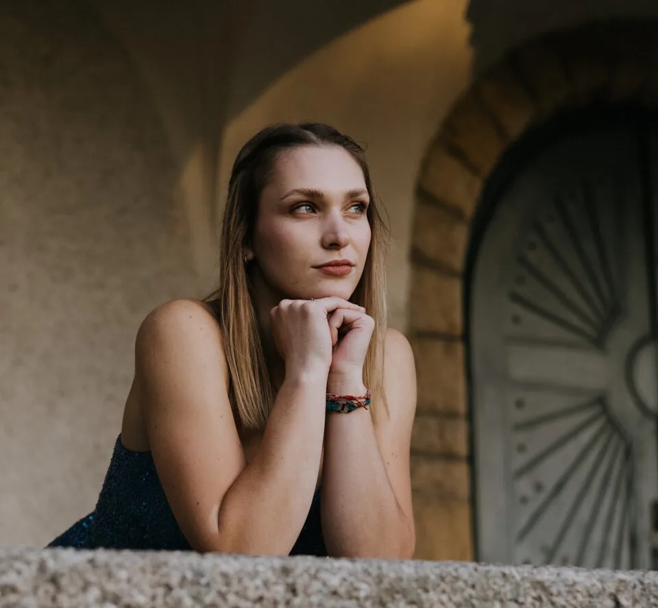 Žena opřená o kamennou římsu před klenutými dveřmi